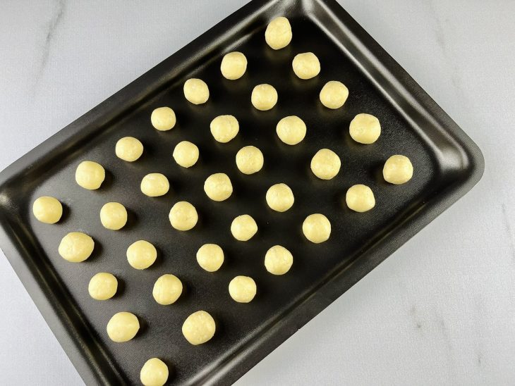 Biscoitos modelados em formato de bolinhas sobre a assadeira.