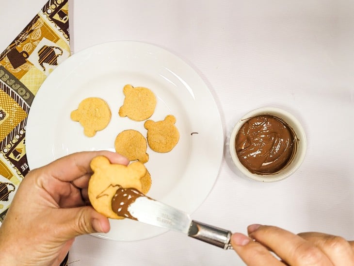 Biscoitinhos assados sendo decorados com chocolate derretido.