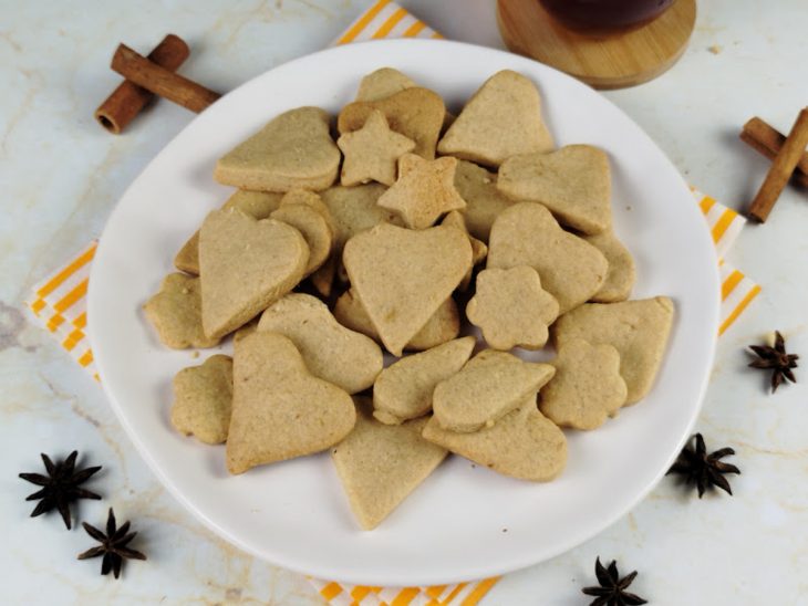 Foto composta por um prato com biscoitos amanteigados e uma xícara de vidro com chá.