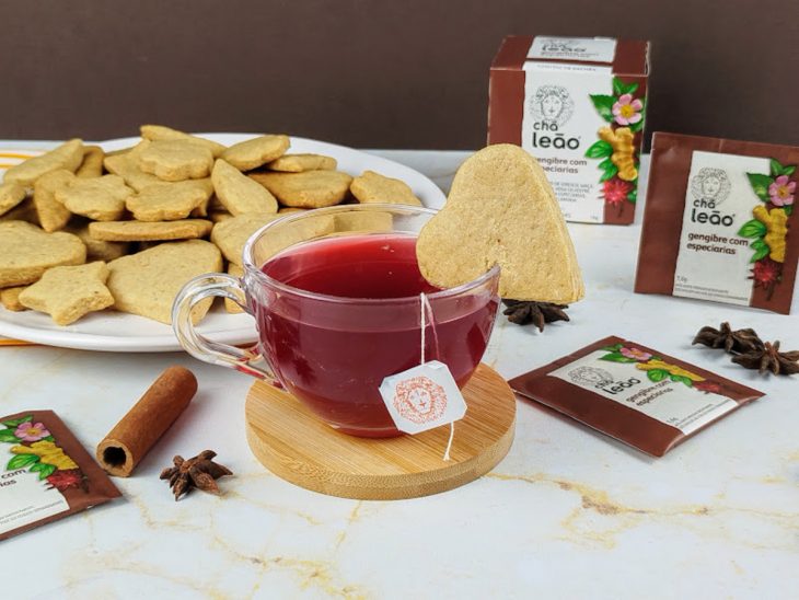 Foto composta por um prato com biscoitos amanteigados e uma xícara de vidro com chá.