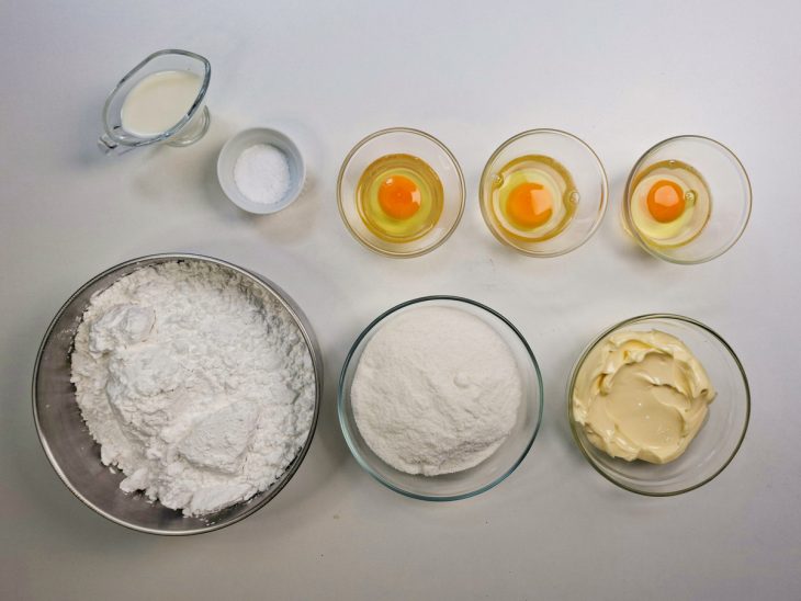 Ingredientes organizados na bancada com ovos quebrados em recipiente.