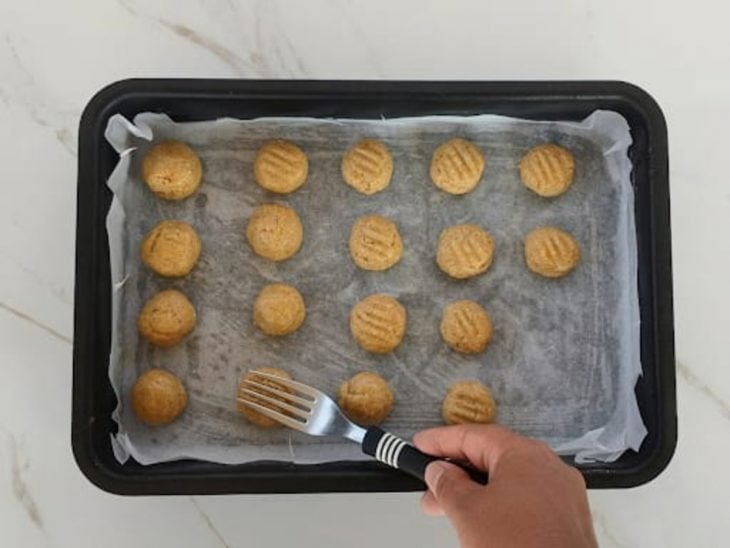 Bolinhas sendo pressionadas com um garfo formando os biscoitos.