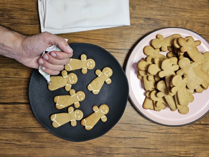 Mão decorando os biscoitos com chocolate branco dentro da bisnaga.