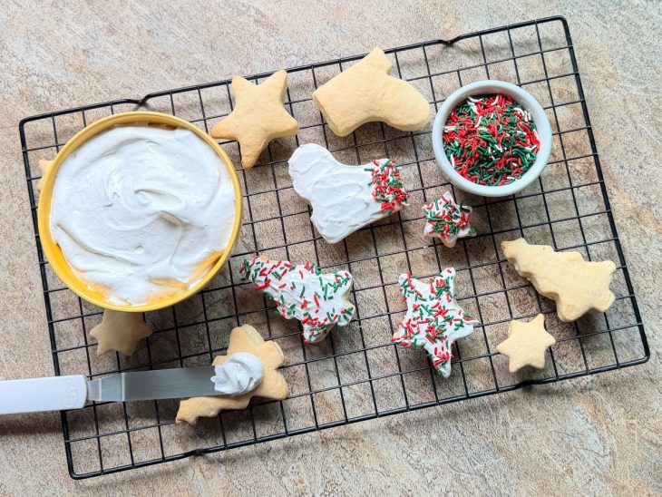 Biscoitos frios sendo decorados com glacê e granulado colorido.