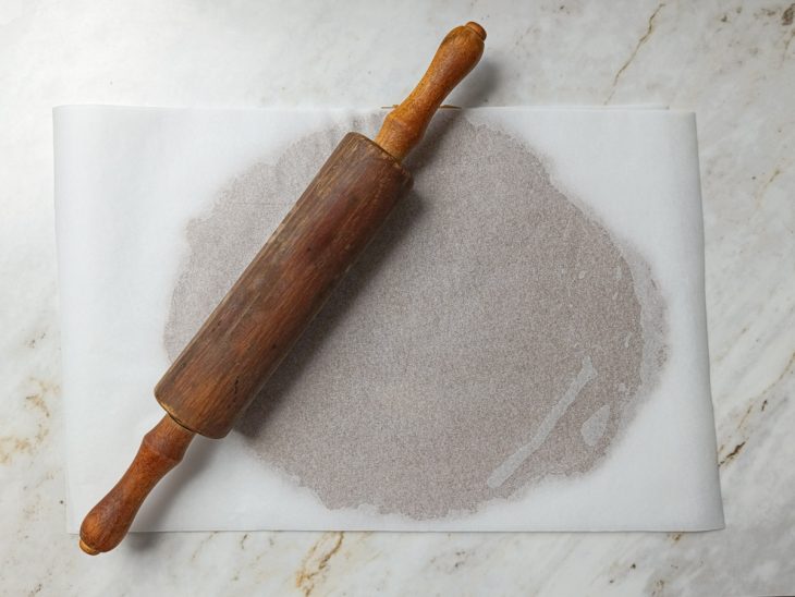 Massa aberta entre papéis manteiga com auxílio de um rolo.