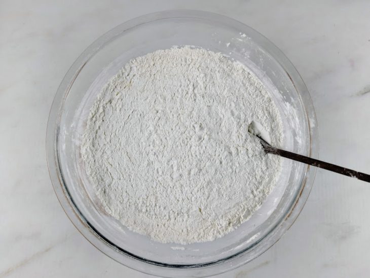 Polvilho doce, amido de milho, farinha de trigo, açúcar, fermento e sal misturados em uma tigela de vidro.