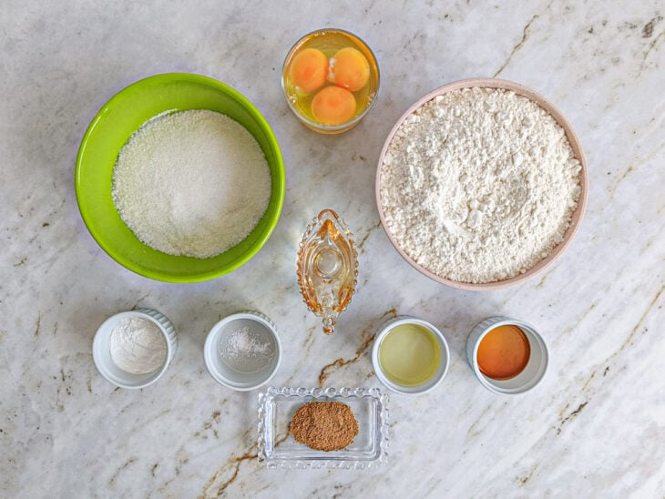 Ingredientes organizados na bancada com ovos, farinha, açúcar, óleo, vinagre e demais ingredientes da receita.