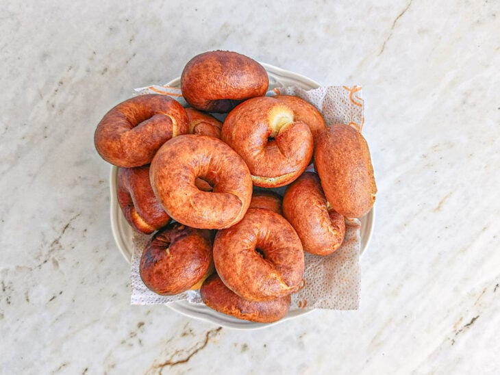 Biscoitos dourados sendo retirados com uma escumadeira e colocados sobre papel-toalha.