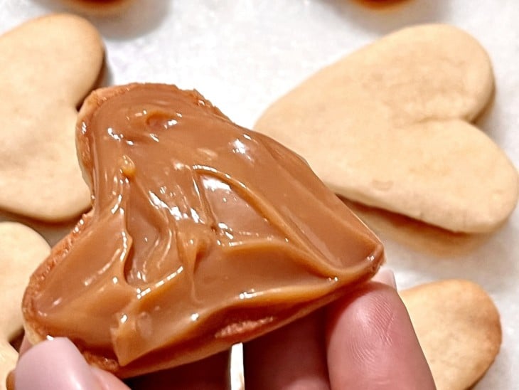 Um biscoito sendo recheado com doce de leite.