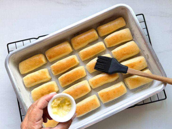 Manteiga sendo pincelada sobre os pãezinhos.