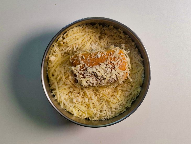 Bisnaguinha sendo empanada na mistura de panko com queijo ralado.