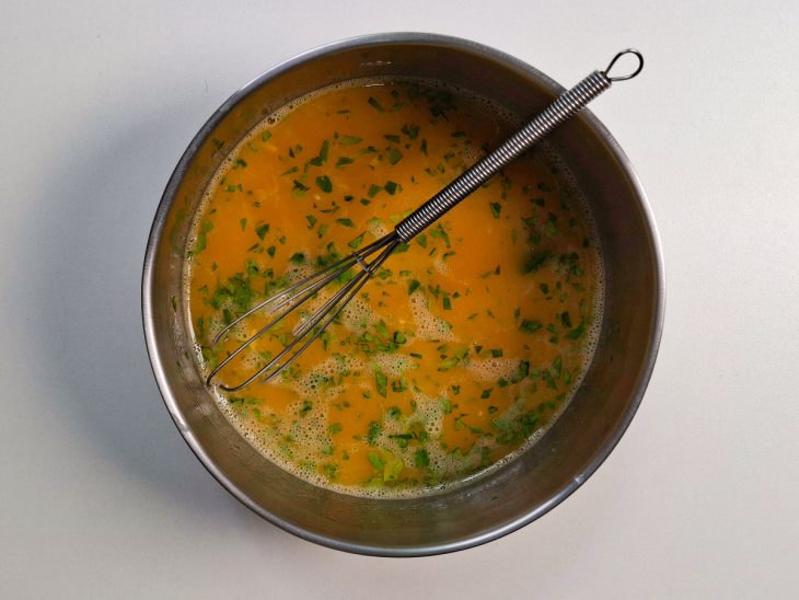 Mistura de manteiga, alho, ovos e salsinha sendo batida com fouet.