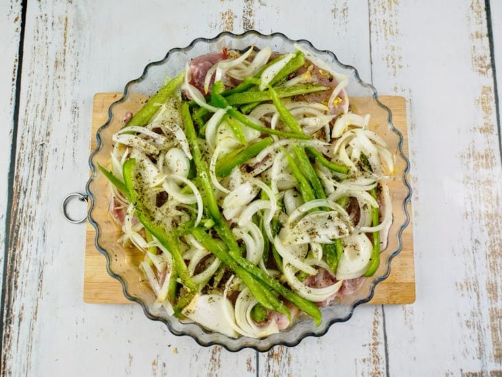Ingredientes colocados sobre as bistecas, regados por azeite e finalizados com orégano.
