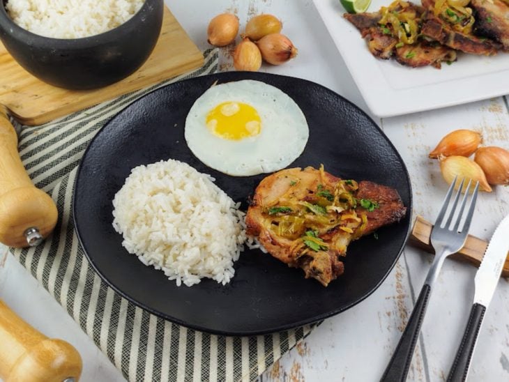 Bisteca assada pronta para consumo, servida com arroz e ovo.