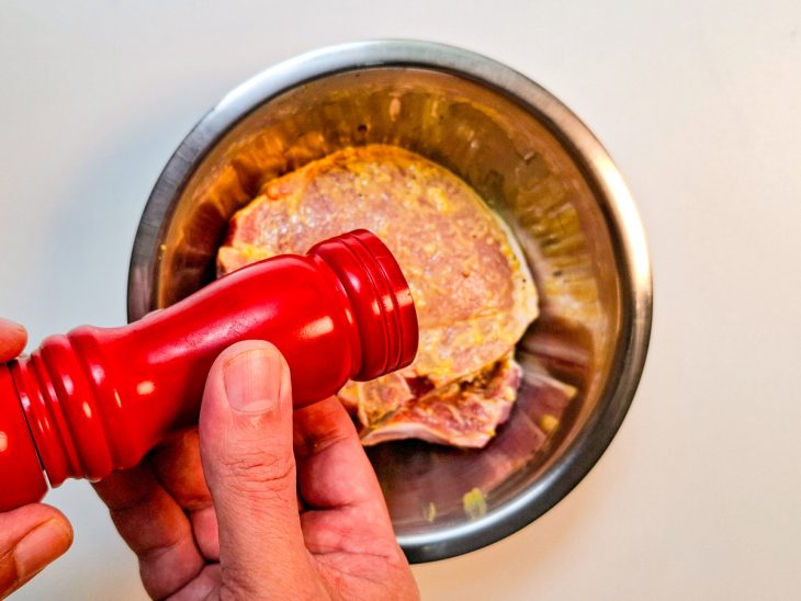 Numa tigela, as bistecas temperadas com sal, pimenta-do-reino, alho e mostarda.