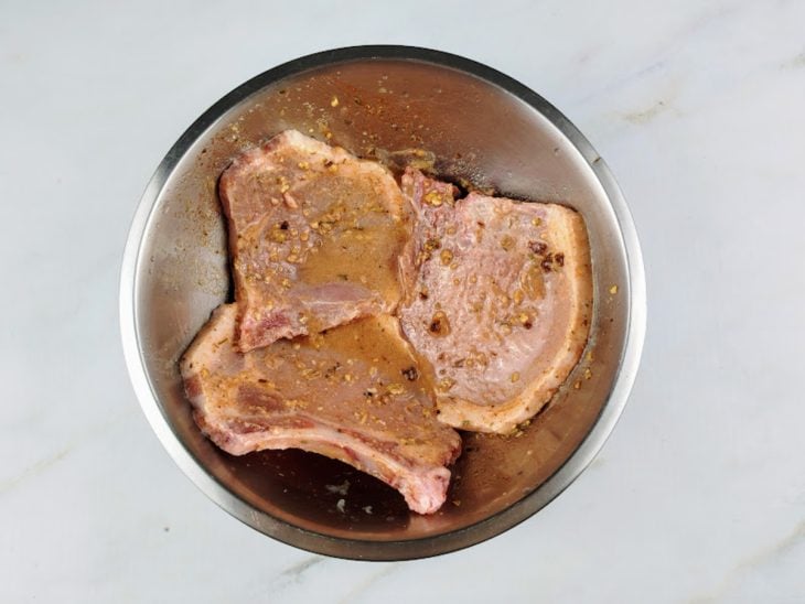 Bistecas em uma tigela com temperos para marinar.