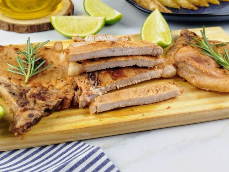 Bistecas de porco fatiadas e prontas para consumo, acompanhada por limões e batatas.