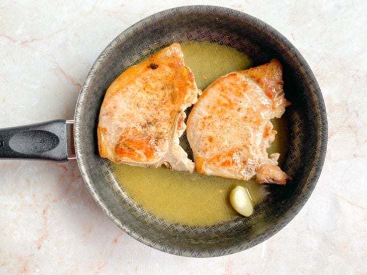 Uma frigideira com as bistecas, manteiga, alho e suco de limão.