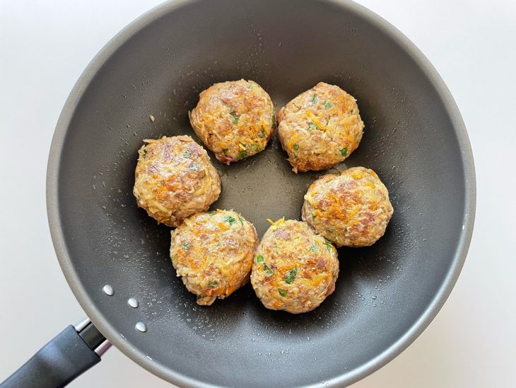 Bolas de carne grelhando numa frigideira.