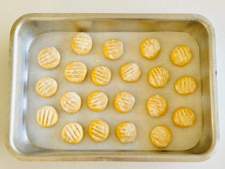 Bolinhas achatadas de massa dispostas na forma e marcadas com garfo.