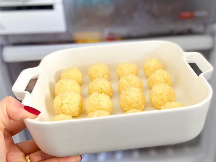 Uma assadeira com bolinhas de queijo cruas no congelador.
