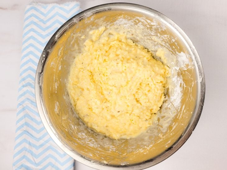 Um recipiente contendo a mistura de ovos batidos, polvilho, o queijo minas ralado, o sal e o orégano.