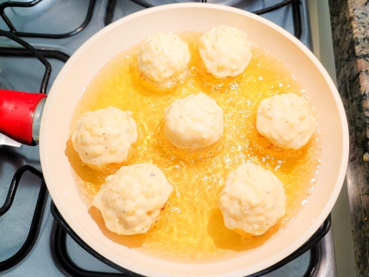 Uma frigideira com óleo fritando bolinhas de queijo.