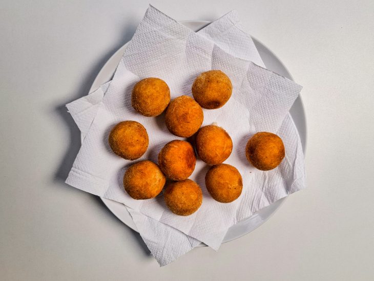 Bolinhas de queijo fritas sobre um prato forrado com papel-toalha.