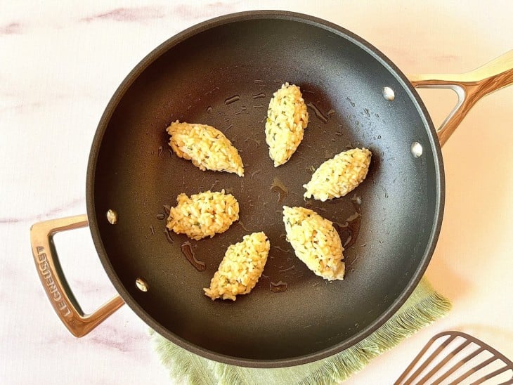 Uma frigideira com alguns bolinhos de arroz refogando no azeite.