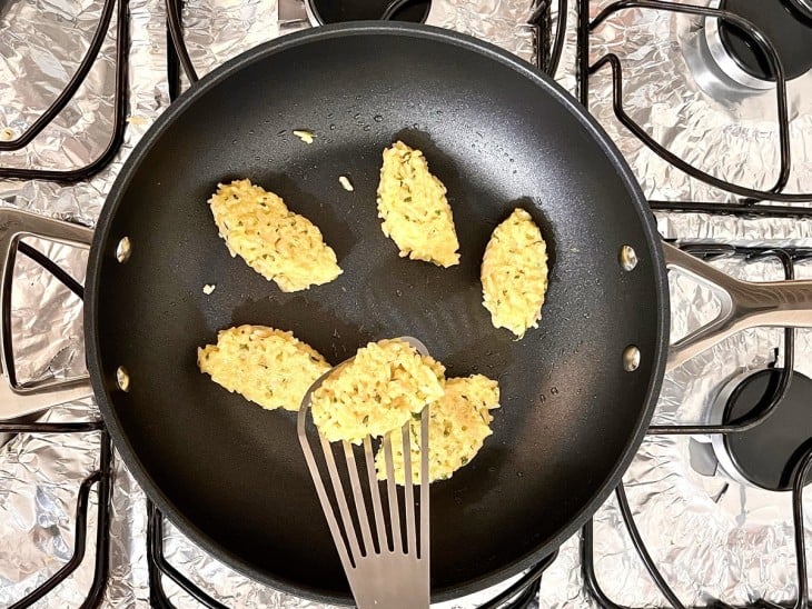 Uma frigideira com alguns bolinhos de arroz refogando no azeite.