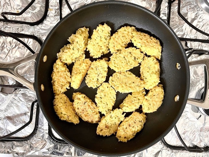 Uma frigideira com alguns bolinhos de arroz refogando no azeite.