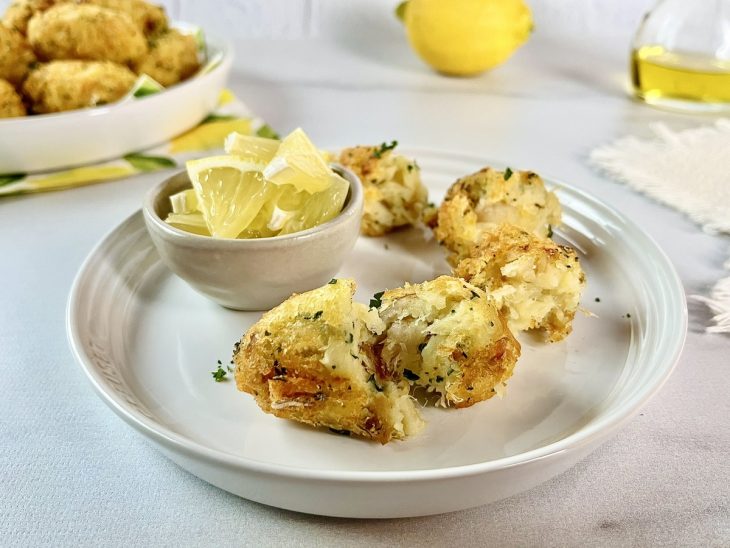 Bolinhos de bacalhau, servidos em prato, com acompanhamento de rodelas de limão.