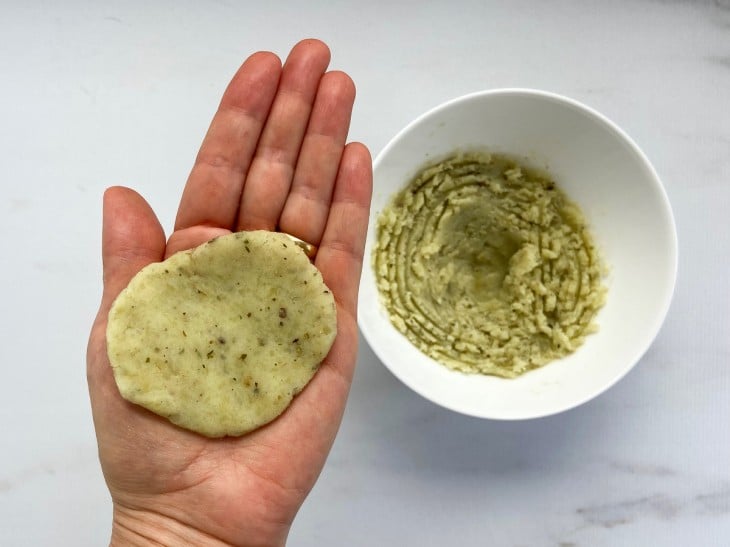 Uma porção da massa de batata amassada aberta na palma da mão.