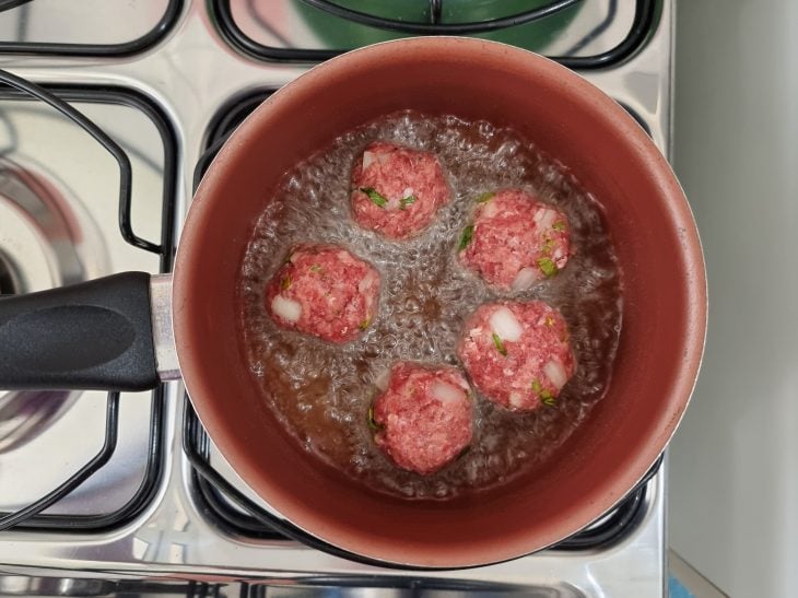 Bolinhas de carne moída fritas em óleo quente na panela.