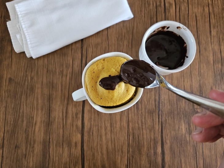 Calda sendo adicionada por cima do bolinho de cenoura fit na xícara.