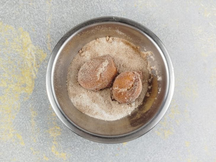 Bolinhos sendo passados na mistura de açúcar com canela.