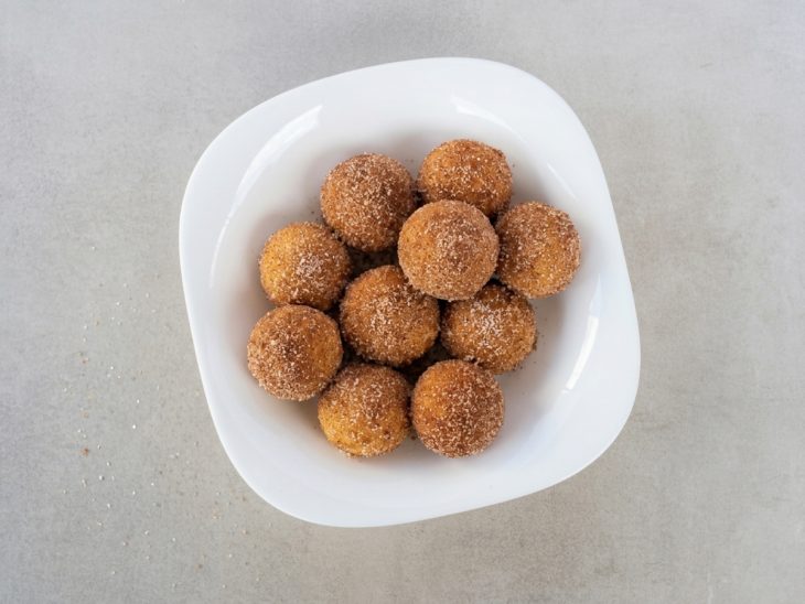 Bolinhos ainda mornos sendo envolvidos em açúcar com canela.
