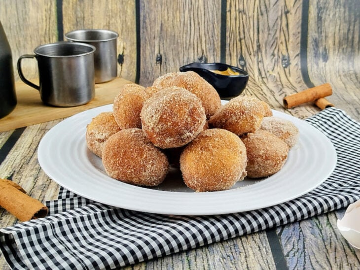 Bolinhos de chuva servidos em uma travessa ao lado de uma xícara de café.