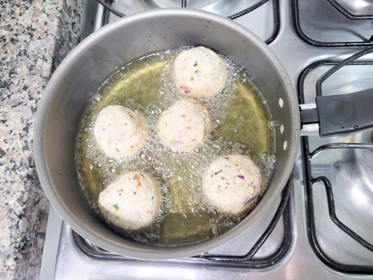 Uma panela com óleo quente fritando os bolinhos.