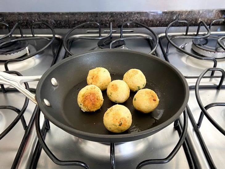 Frigideira com 6 bolinhos de grão-de-bico sendo grelhados.