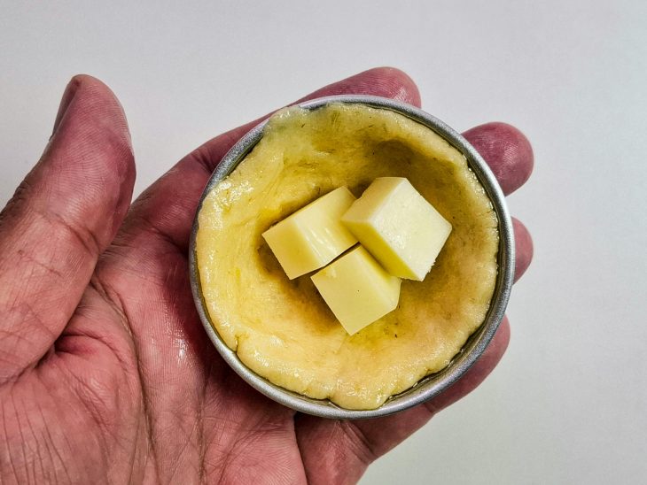 Cubos de queijo adicionados ao meio da forminha forrada com a massa de mandioca.