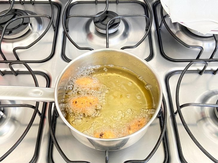 Uma panela com óleo fritando bolinho de peixe.