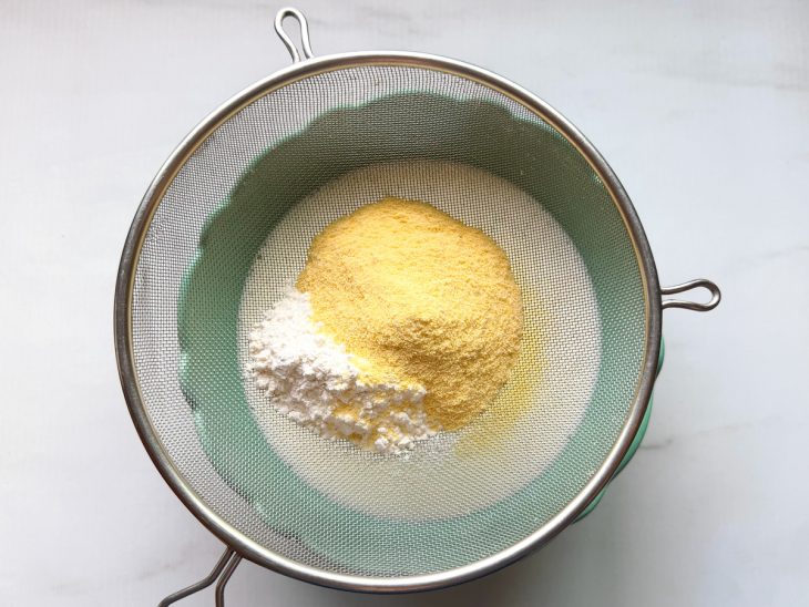 Farinha de trigo e fubá sendo peneirados na tigela.