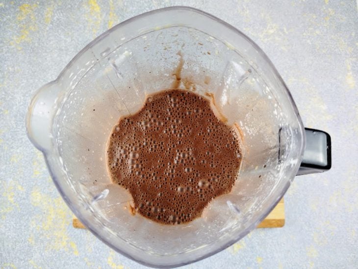 Um liquidificador com ovos, chocolate em pó, farinha, água e açúcar.