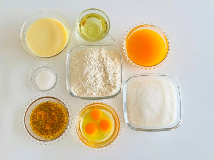 Ingredientes da massa e da cobertura organizados sobre a bancada com maracujá, ovos, farinha e leite condensado.