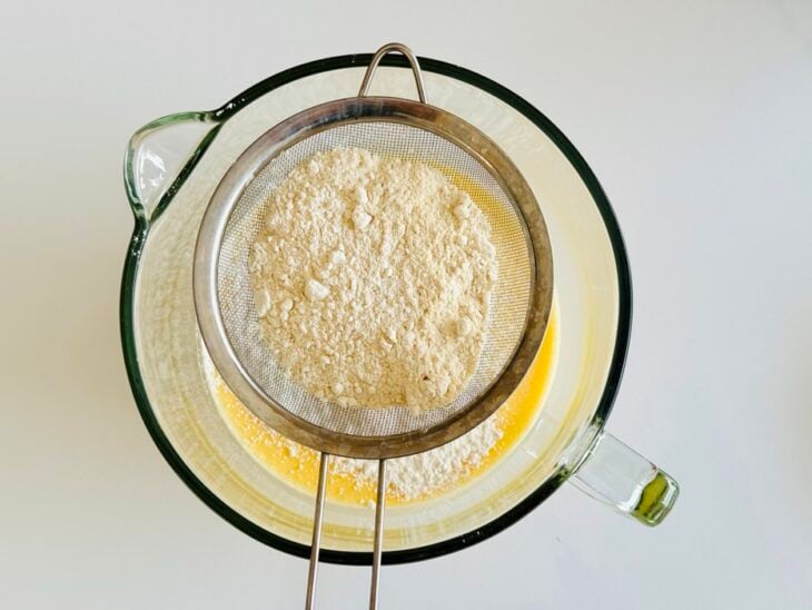 Farinha de trigo peneirada sendo incorporada delicadamente à massa.