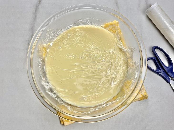 Um prato contendo um creme coberto com plástico filme.