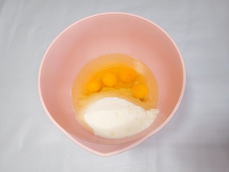 Tigela de cor amarela com ovos, óleo e açúcar.