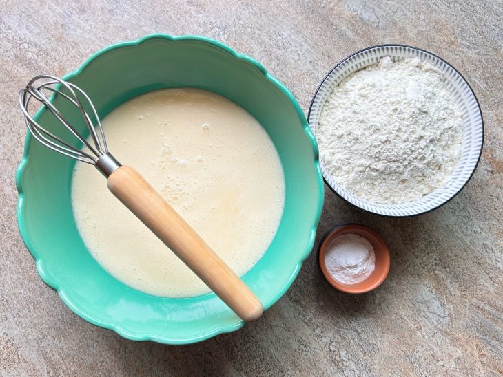 Numa tigela, a mistura do liquidificador, ao lado a farinha e o fermento.