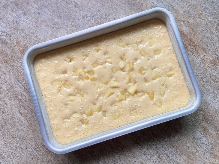 No tabuleiro, a massa com os pedaços de abacaxi.